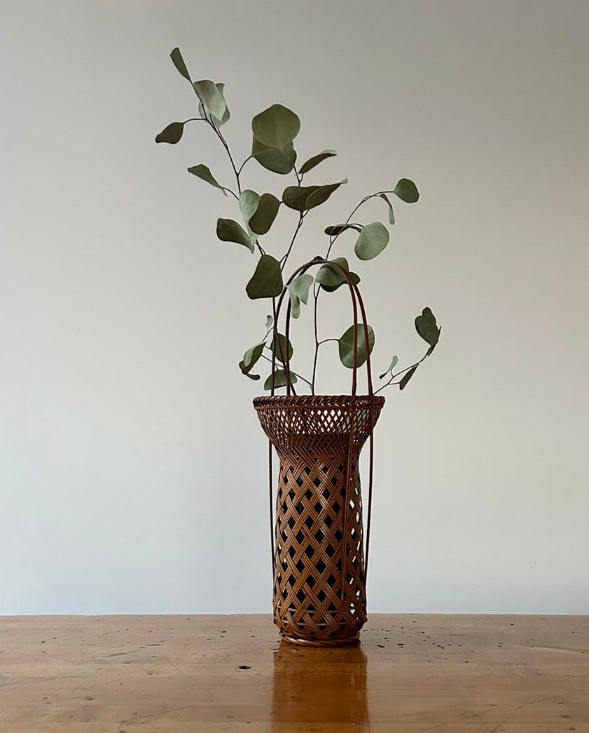 A vintage Japanese Ikebana (flower arrangement) basket with handle. Woven by hand in Japan from caramel colored bamboo. Circa 1950.