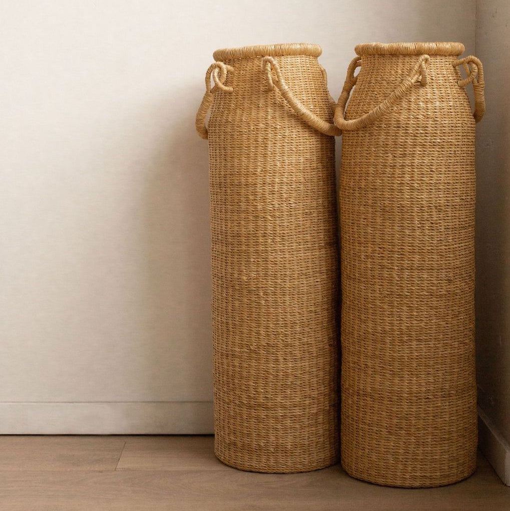 A tall column-shaped baskets with two handles. More sculpture than storage, these handwoven baskets are made in Ghana from natural materials.