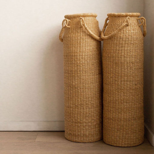 A tall column-shaped baskets with two handles. More sculpture than storage, these handwoven baskets are made in Ghana from natural materials.
