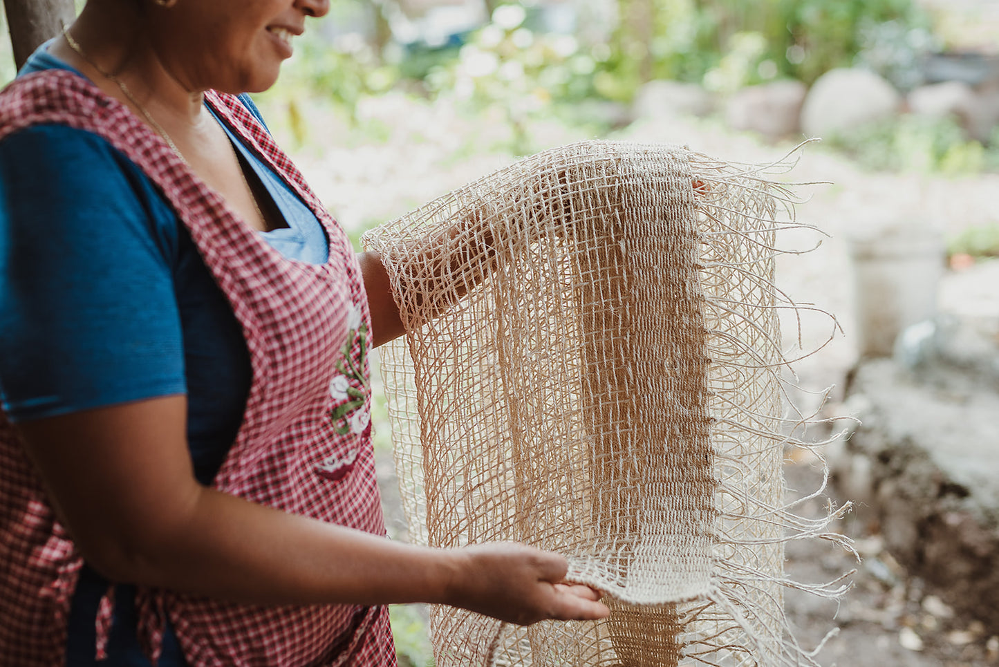 Woman holding our Cortina Maguey, which is a handwoven sheer textile hanging. It's made in Oaxaca, Mexico, from the leftover maguey leaves from mezcal production. These natural colored curtains make beautiful room dividers, window coverings or wall hangings, and can be custom made to any size.