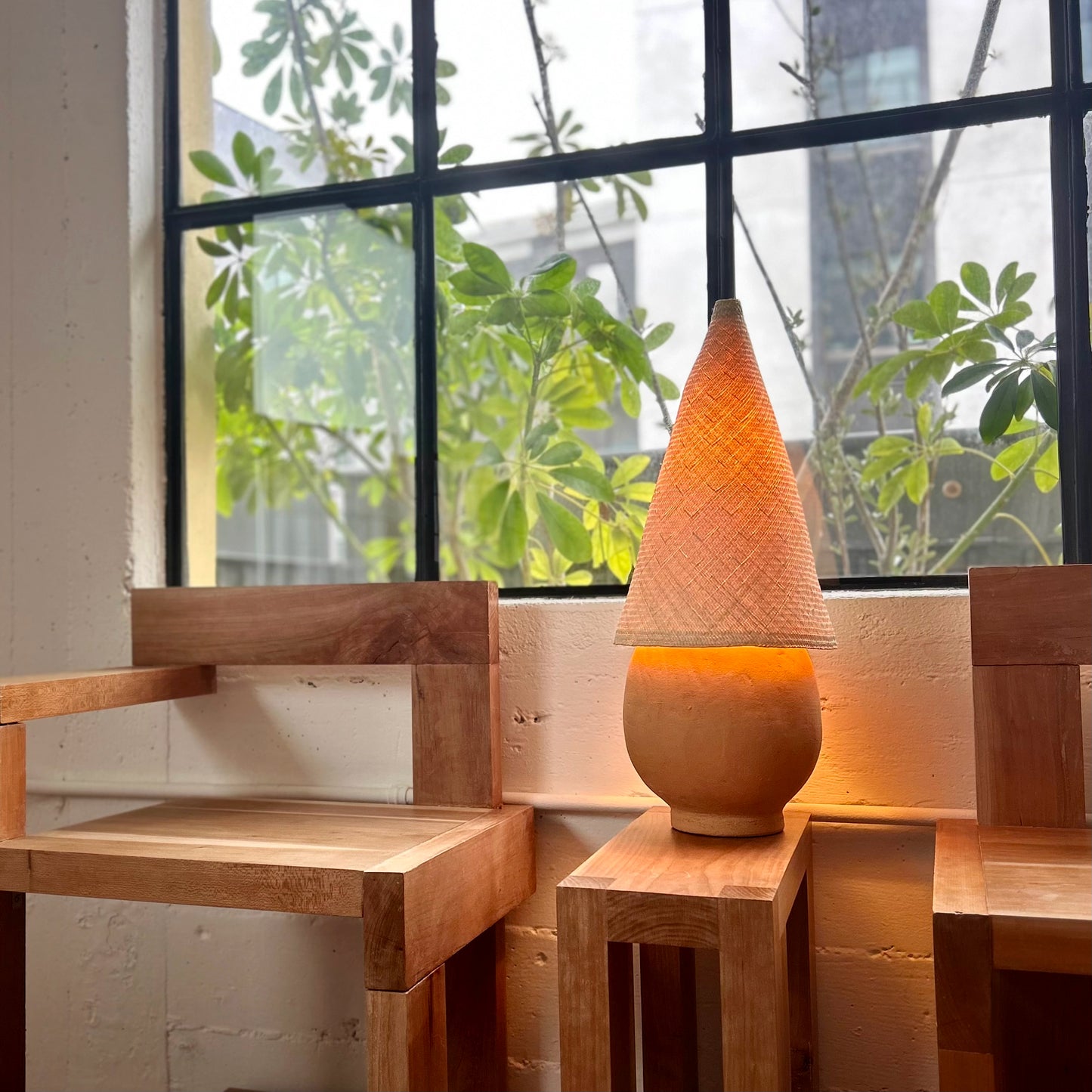 The Duende Lamp has a handcrafted, round, terracotta colored, ceramic base, with a natural colored, pointed cone shaped, hand woven, dried palm leaf lampshade.
