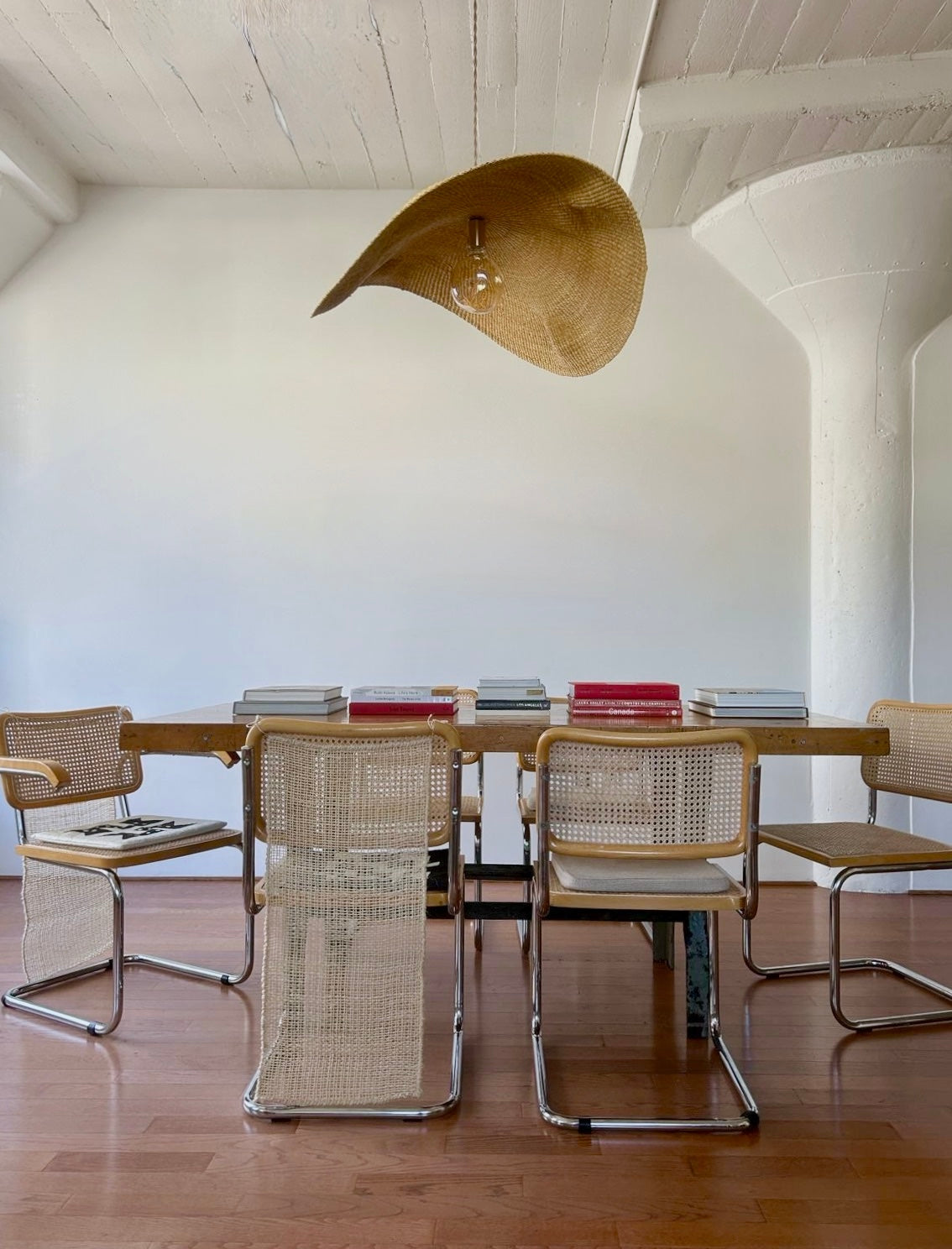The hand woven, natural colored Fawn pendant light is shown over a dining table and chairs.