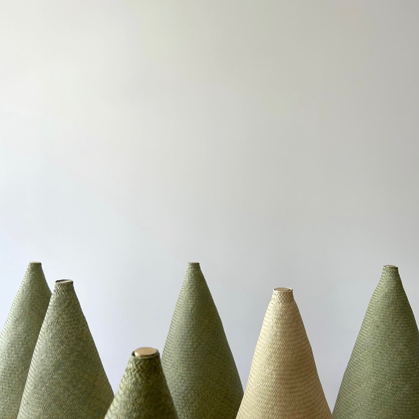 Showing the tops of multiple Duende Lamp’s pointed cone shaped, hand woven, dried palm leaf lampshade.