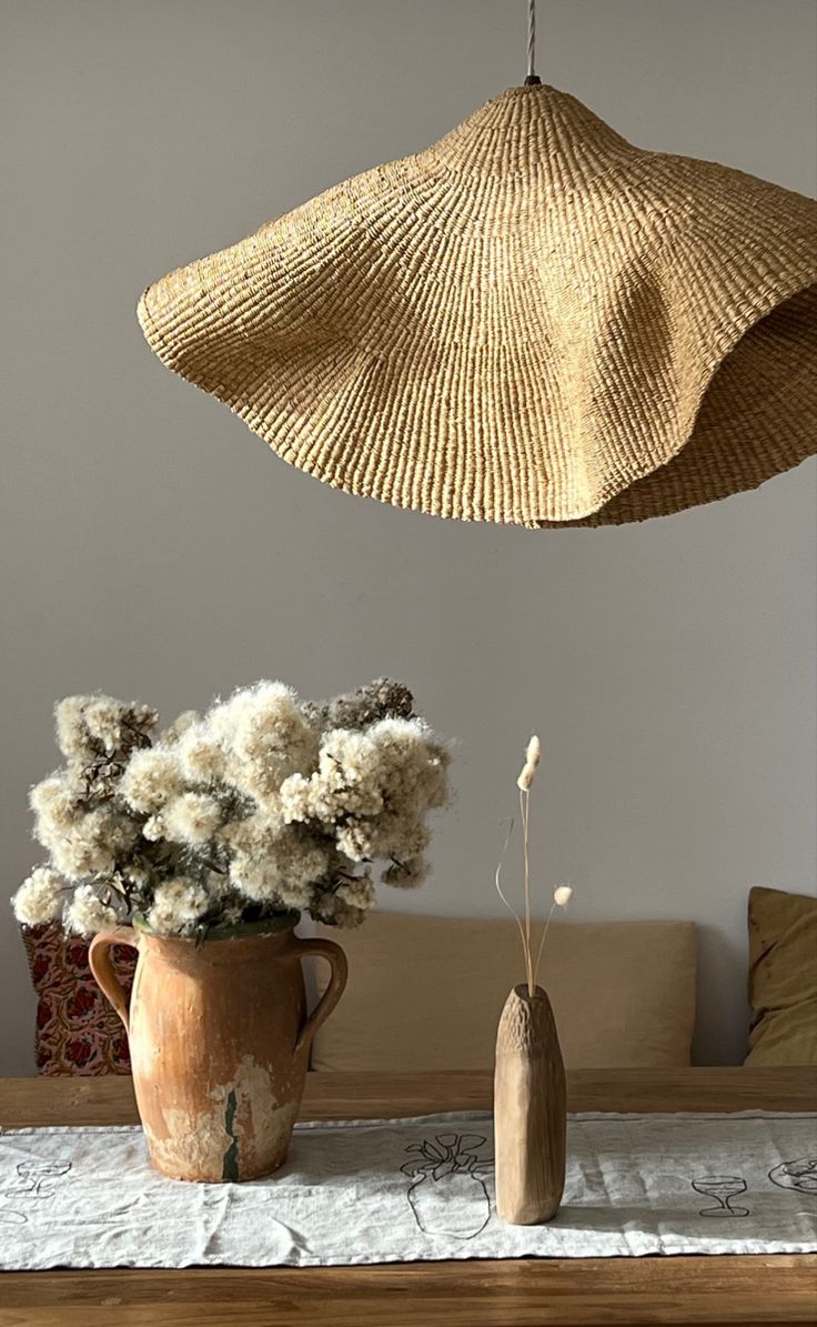 Peaked Fawn light shade over a table, handwoven from sustainable elephant grass in Ghana. Their wide and floating shape are striking in any living space, especially in bedrooms or over dining tables.