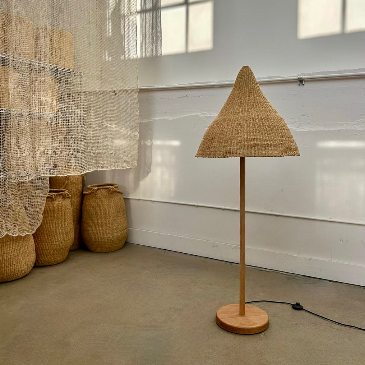 Witches Hat light shade on a floor lamp. Shade handwoven from sustainable materials in Ghana. Their steep cone shape casts a downward light, ideal for spaces that call for a more direct light source.