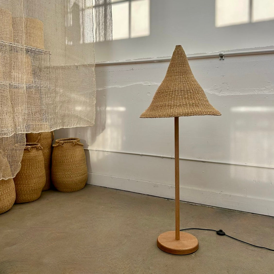 Floor lamp with woven shade, shade is handwoven from sustainable materials in Ghana. They are a steep cone shape. 