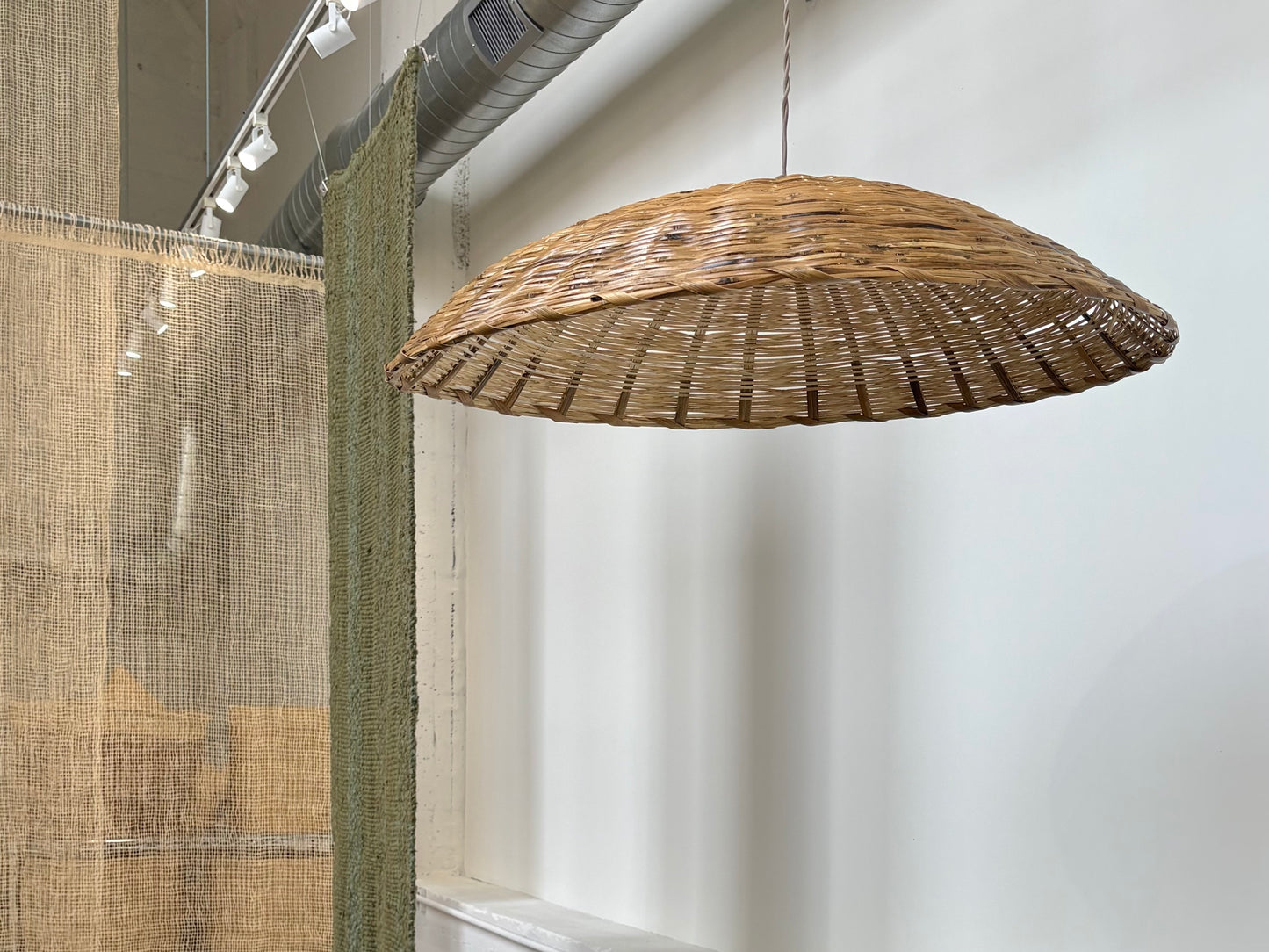 Wicker pendant light hanging from a ceiling in a room with a white wall.