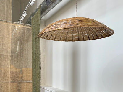 Wicker pendant light hanging from a ceiling in a room with a white wall.