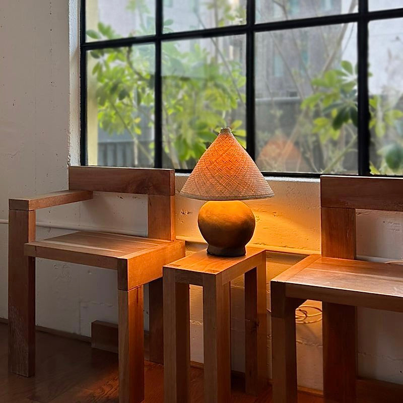 The Ash Lamp has a handcrafted, round, terracotta colored ceramic base and a cone shaped, hand woven, dried palm leaf lampshade - available in either a natural green or blonde colour. 