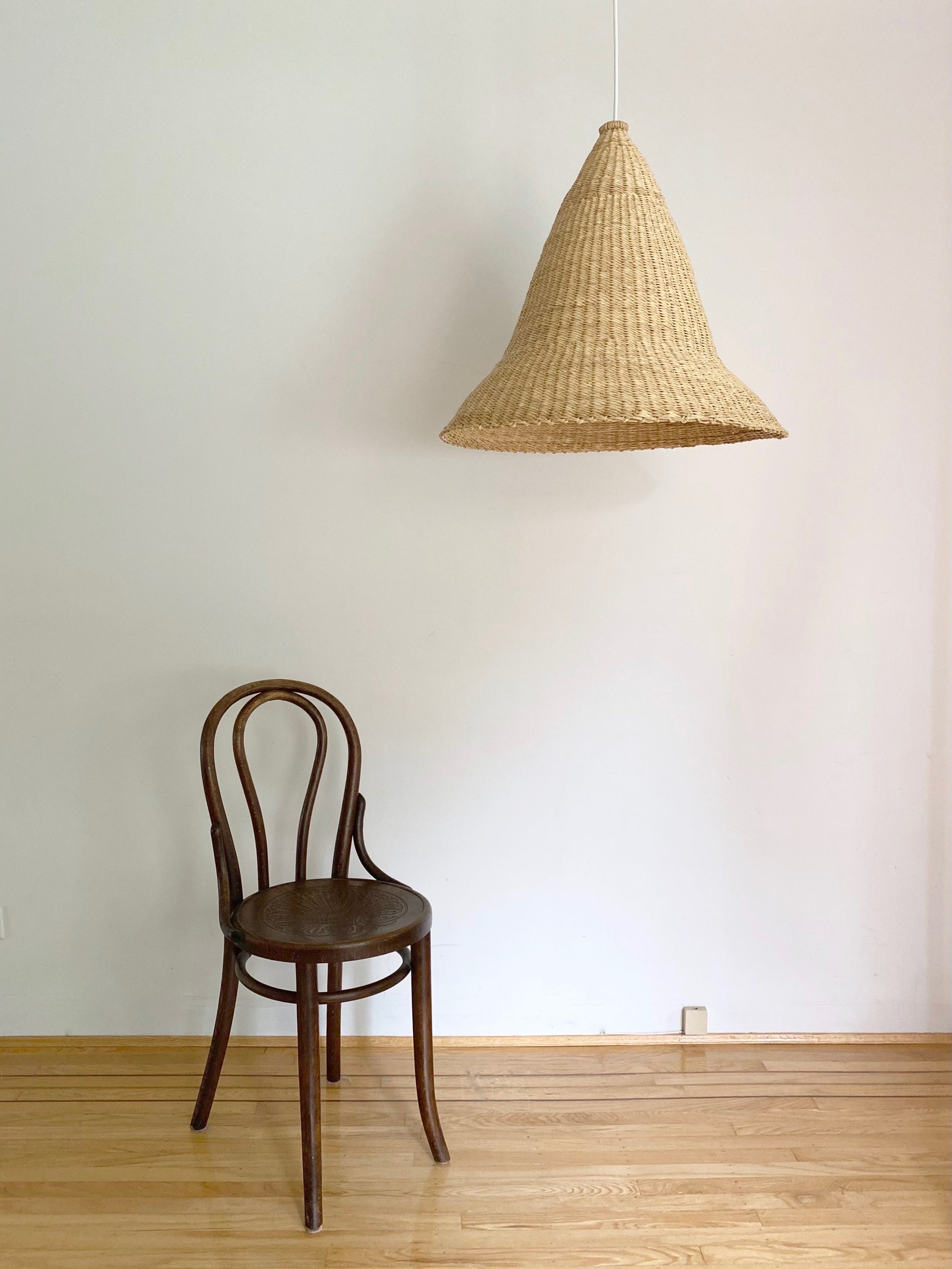 Witches Hat light shade shown with a chair. Shade is handwoven. Their steep cone shape casts a downward light, ideal for spaces that call for a more direct light source.